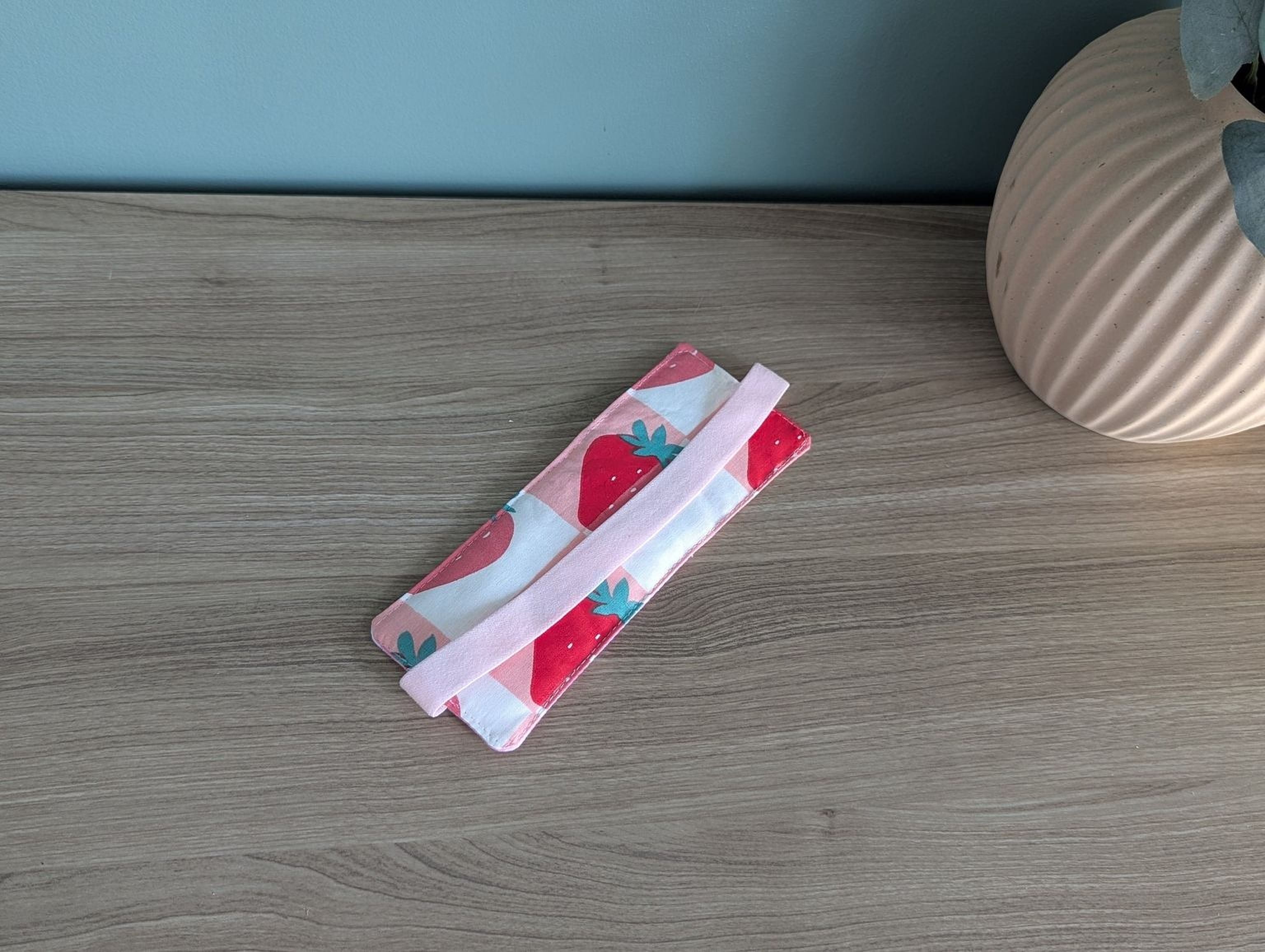 A pink and white striped object, possibly a bag or wallet, is placed on a wooden surface next to a vase.