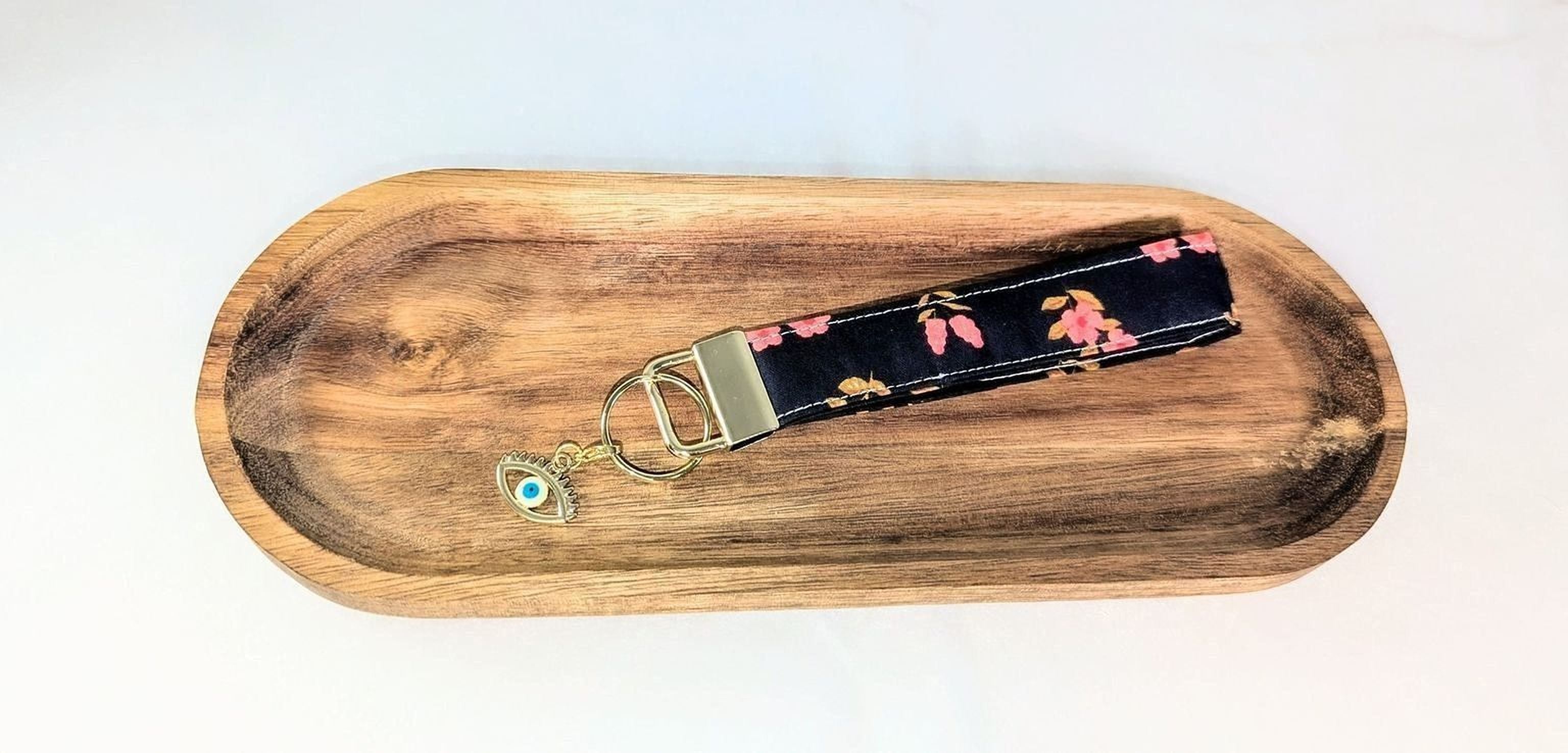 A black and pink floral keychain with a gold-colored metal clasp is placed on a wooden tray.