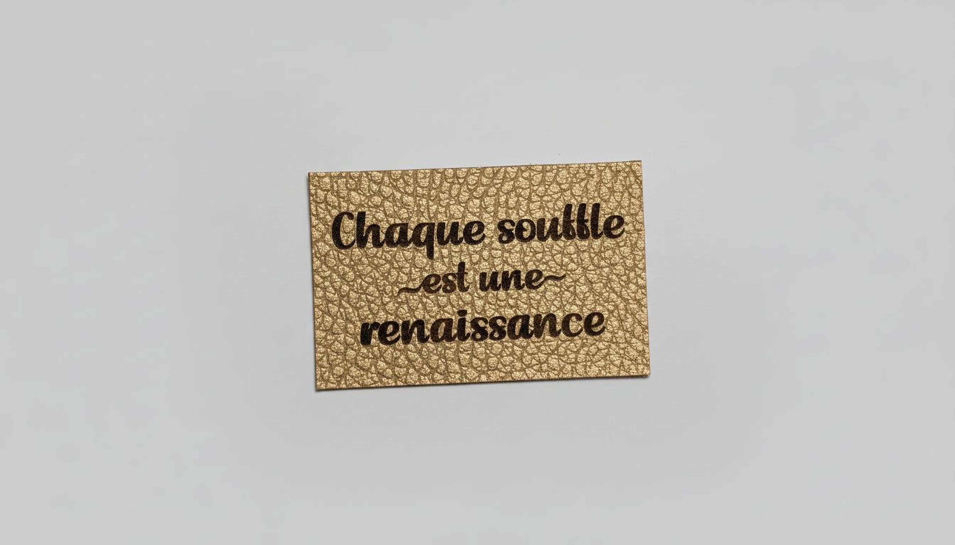 A gold-colored leather tag with the text "Chaque soule est une renaissance" printed on it.
