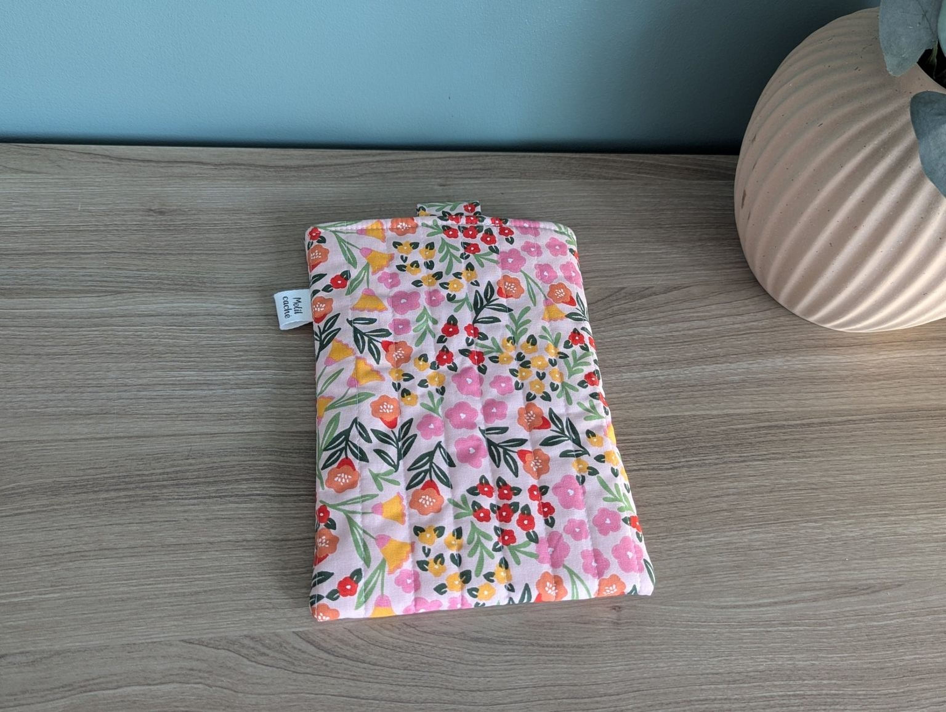 A colorful floral patterned bag or pouch is placed on a wooden surface next to a vase.