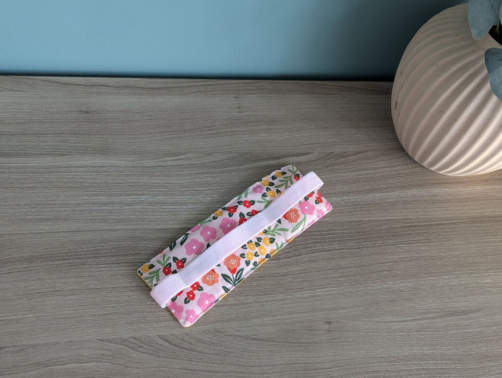 A floral patterned fabric or material with a pink handle is placed on a wooden surface next to a white vase.