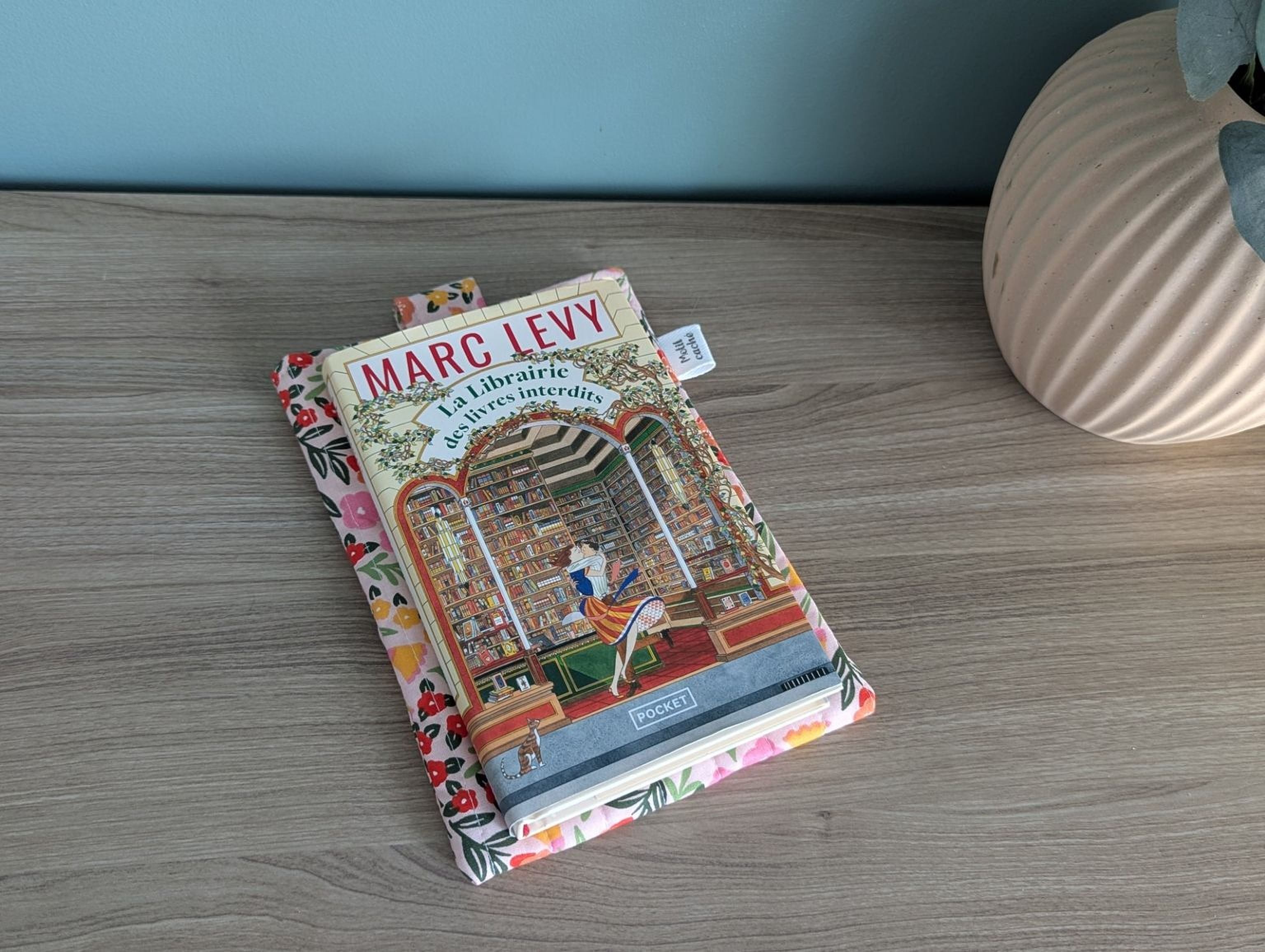 a book titled "Marc Levy" resting on a wooden surface, with a decorative book cover featuring a library scene.