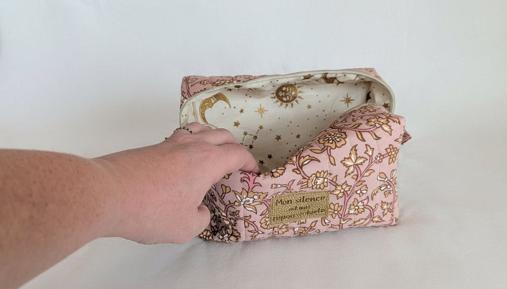 A hand is holding open a pink and gold floral makeup bag with a starry pattern inside.