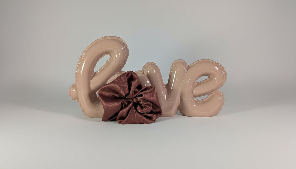 a pink balloon spelling out the word "LOVE" with a brown satin bow placed on top of it.