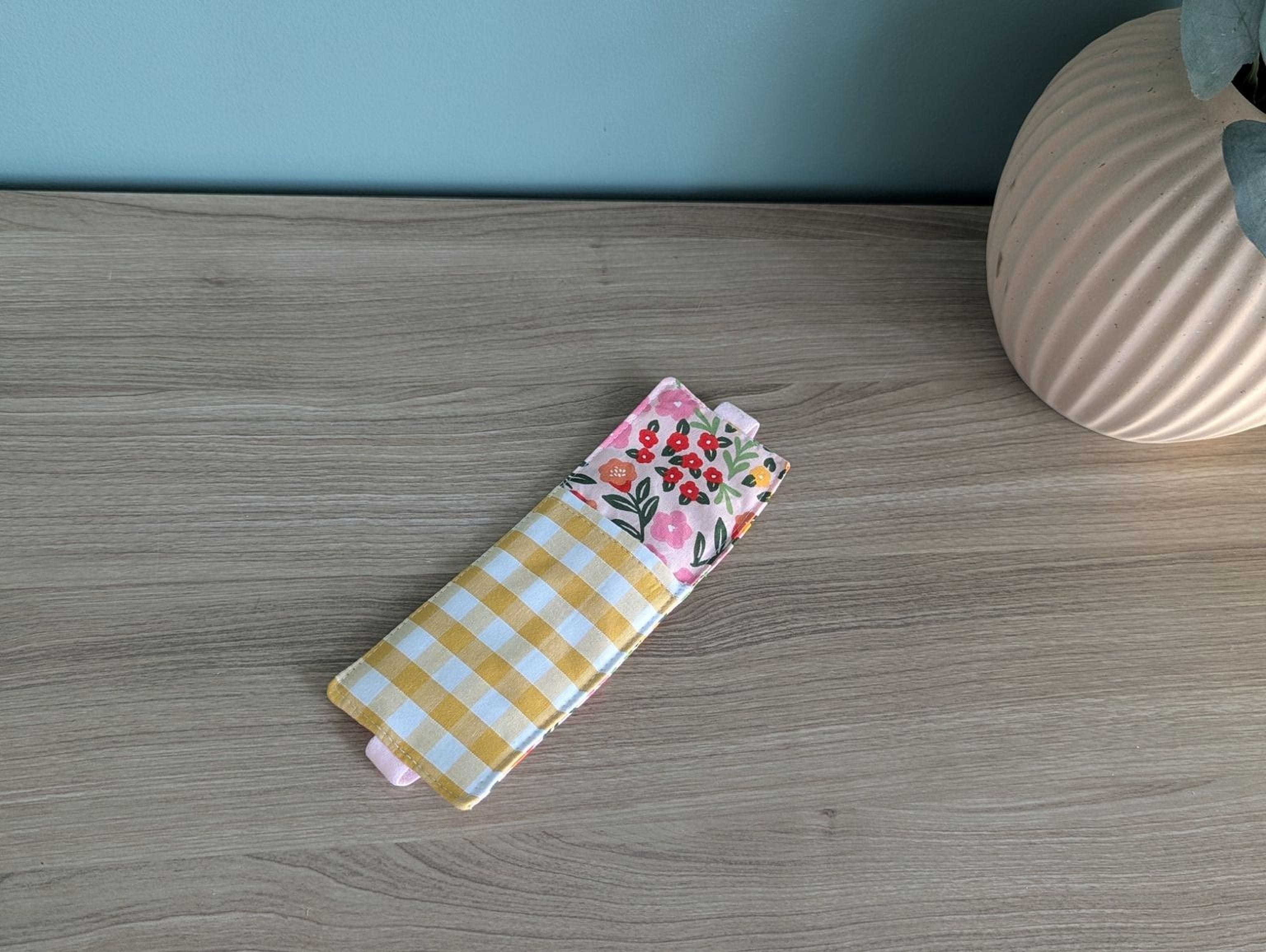 A yellow and white checkered cloth with a floral pattern is placed on a wooden surface next to a white vase.