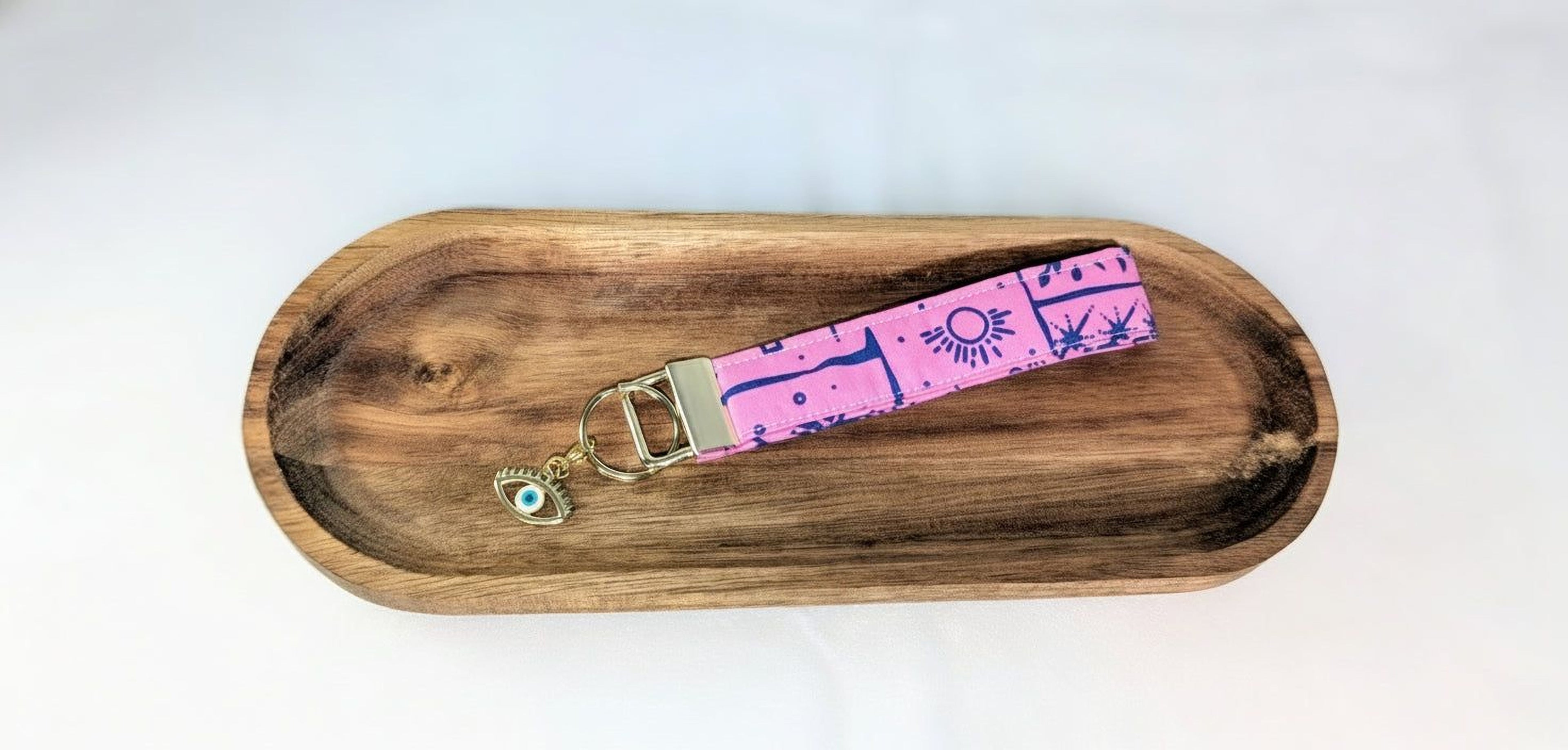 A wooden tray with a pink and blue patterned keychain attached to it.