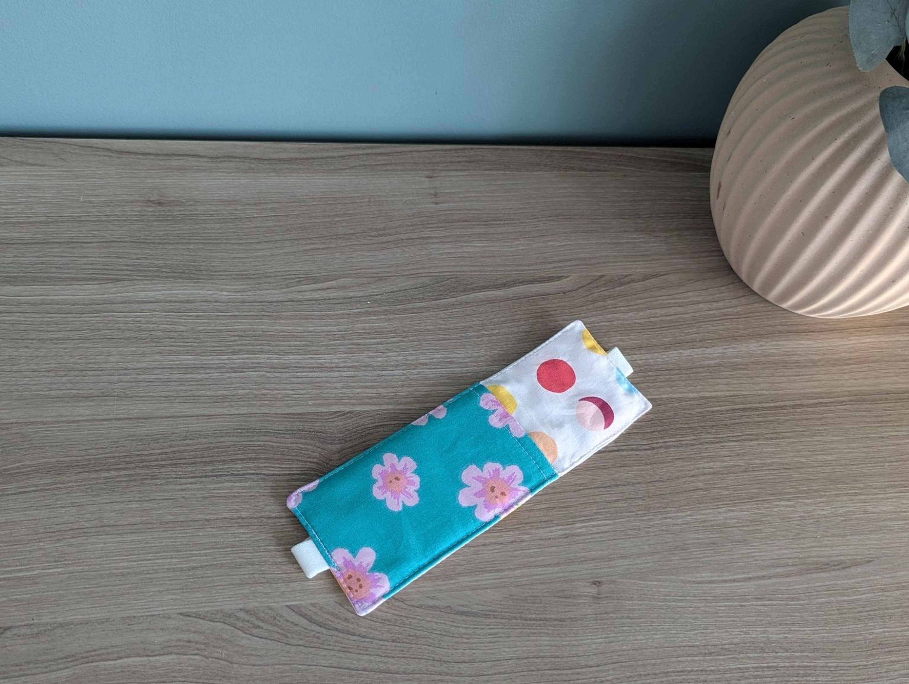A colorful fabric ear pad or pillow is placed on a wooden surface next to a vase.