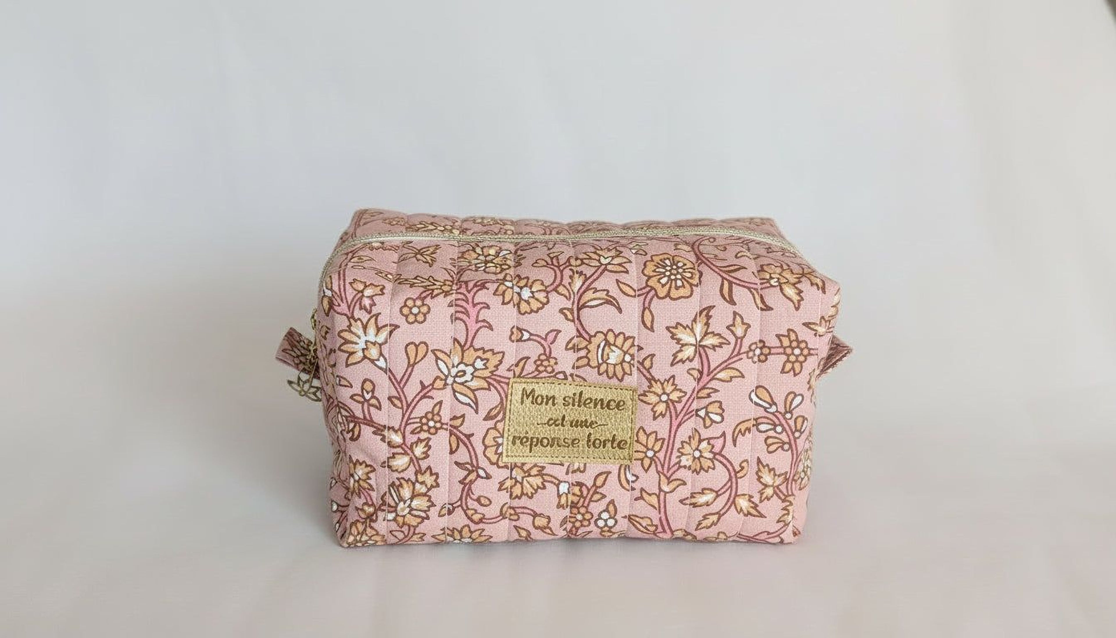 A pink and gold floral patterned bag with a gold label that says "Silence is golden".