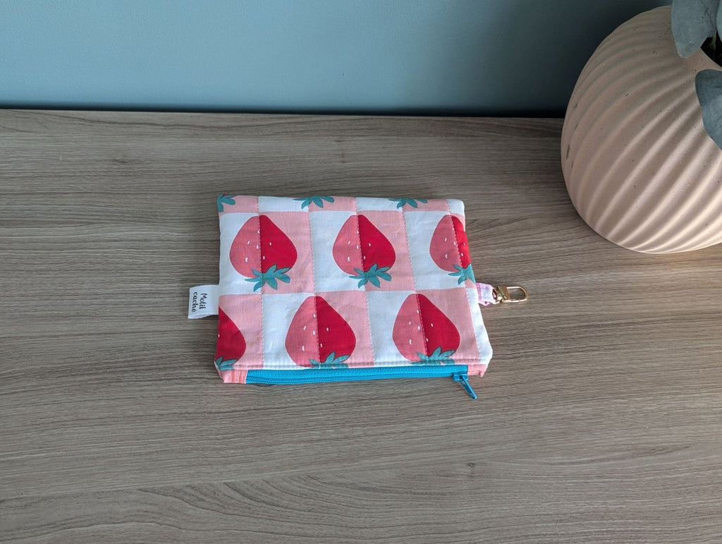A colorful pouch with a strawberry pattern is placed on a wooden surface next to a vase.