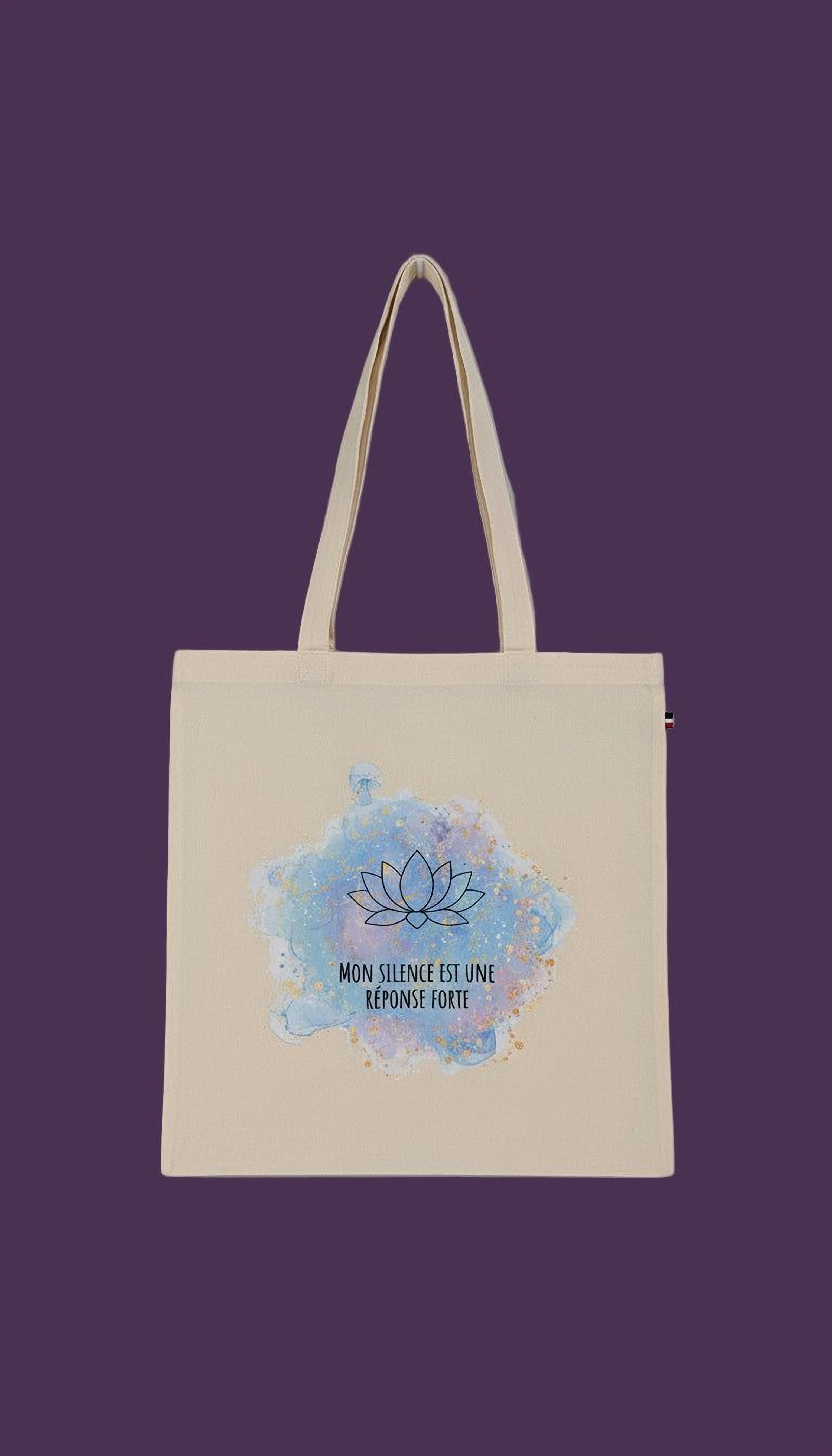 A beige tote bag with a blue and white watercolor design featuring a lotus flower and the text "MON SILENCE EST UMI RESPOSE FORTE" printed on it.