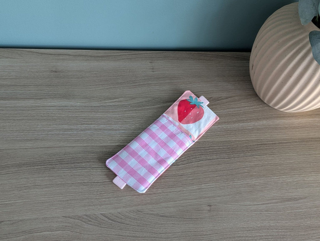 A pink and white checkered cloth with a red heart and a strawberry design is placed on a wooden surface next to a vase.
