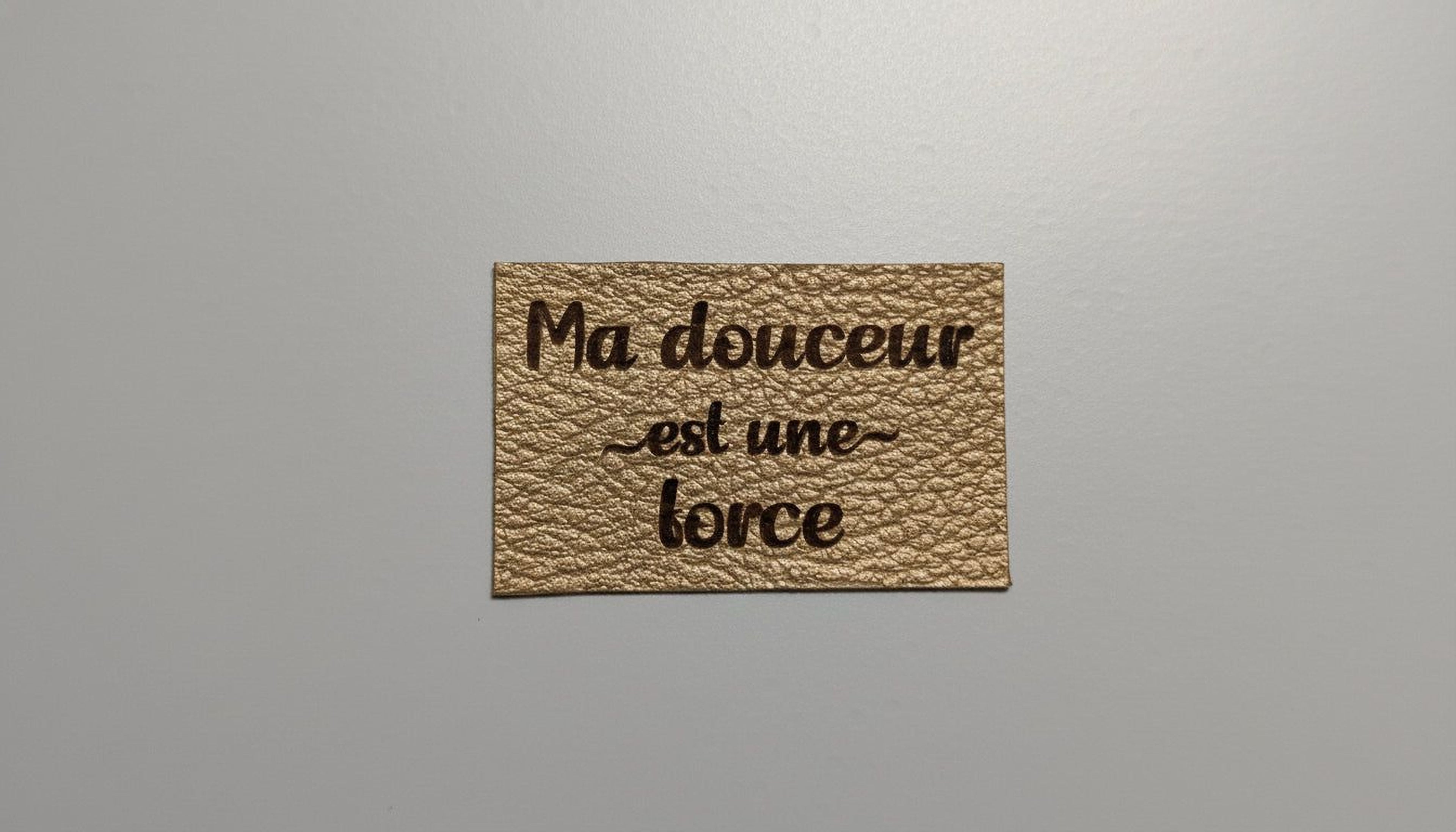 a rectangular piece of leather with the text "Ma ducer est une force" printed on it.