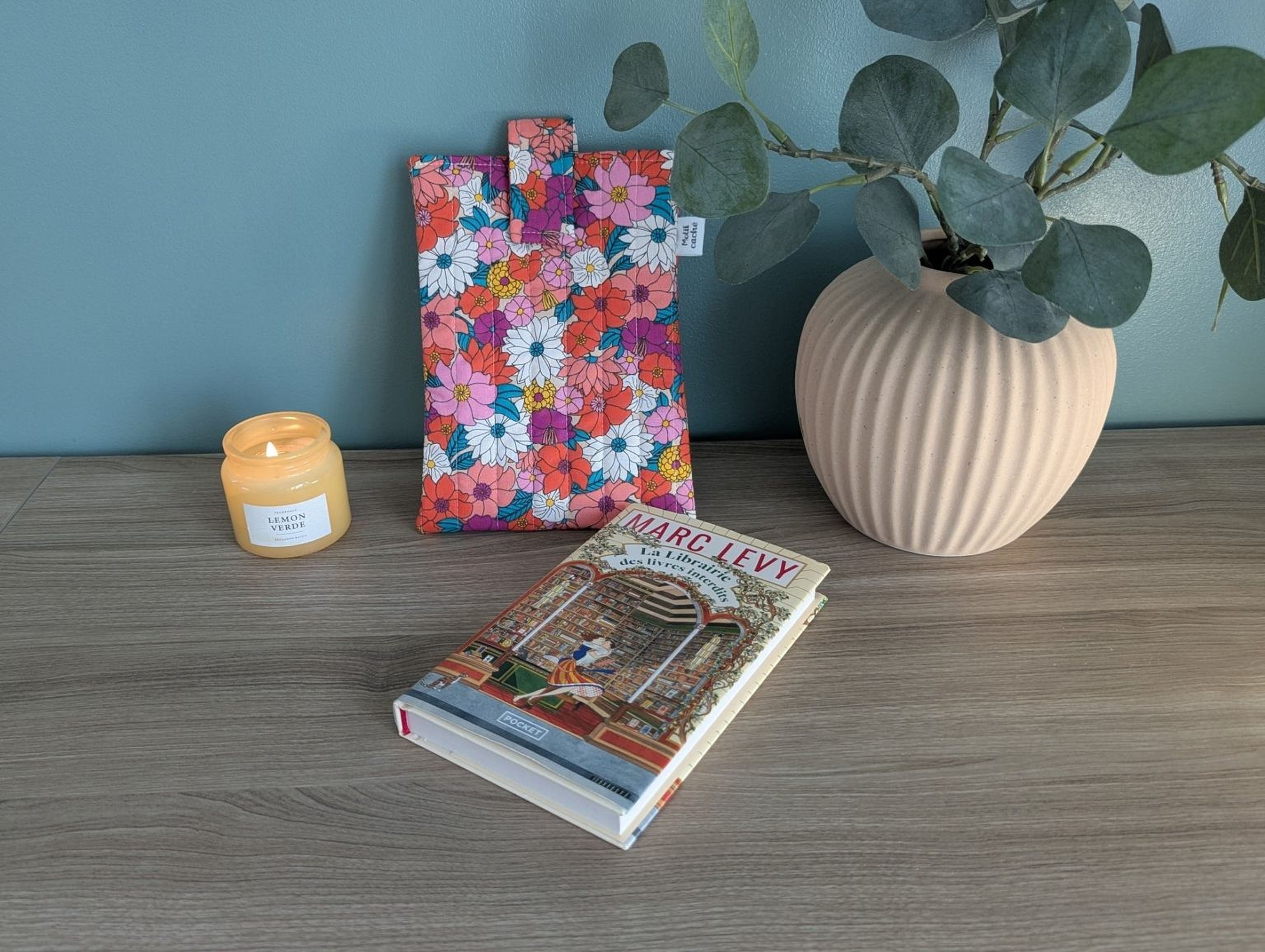 a wooden table with a book, a candle, and a floral bag.