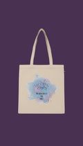 A beige tote bag with a blue and purple watercolor design featuring a lotus flower and the text "MA DOUCEUR EST MÈS FÈRCE" (which means "The flower is the force" in French).