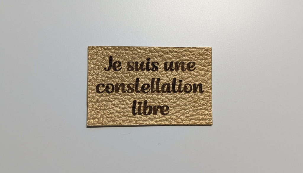 a rectangular, gold-colored piece of paper with the text "Je suis une constellation libre" printed on it.