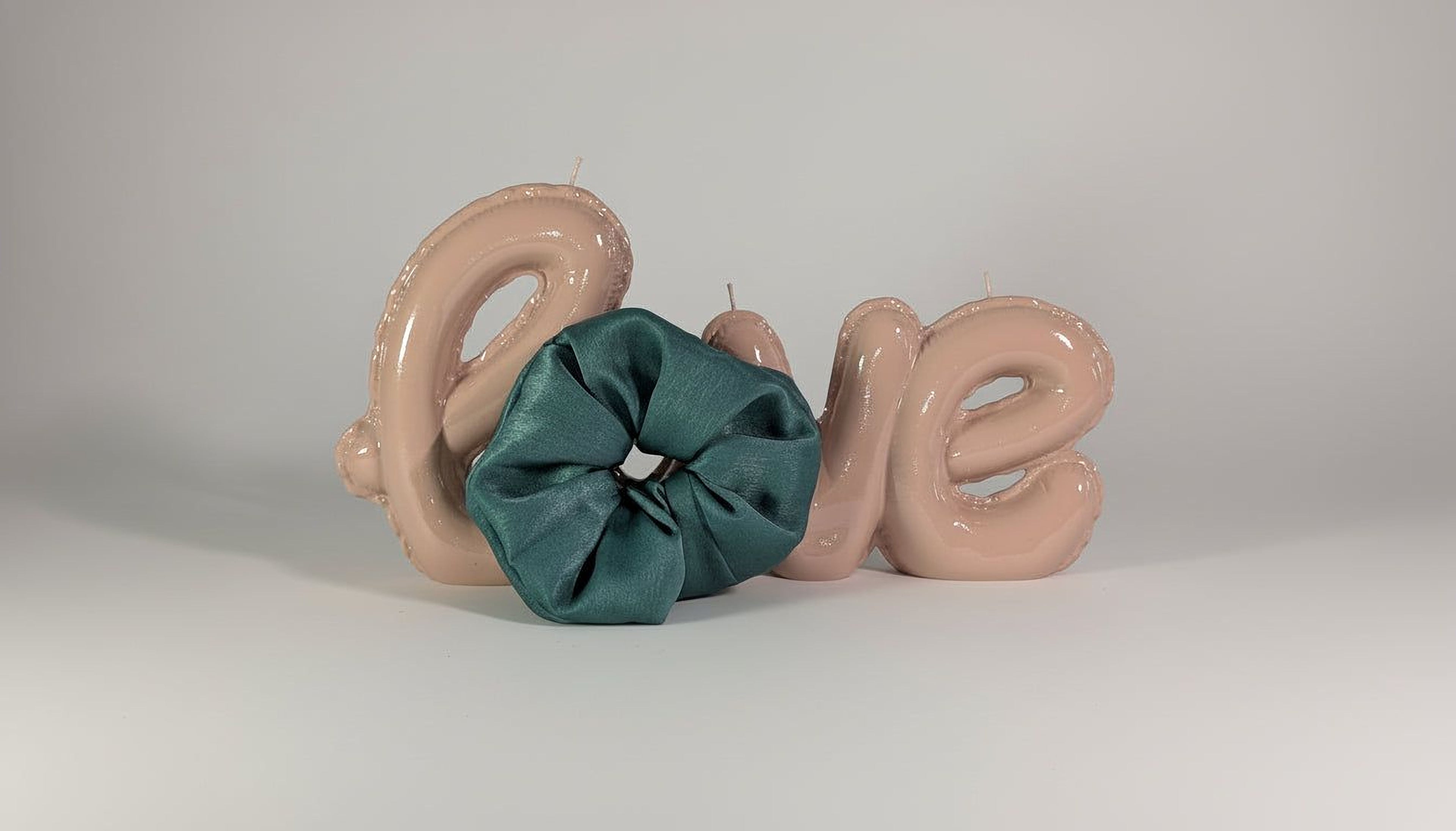 a green scrunchie and two pink balloons spelling out the word "LOVE" on a plain white background.