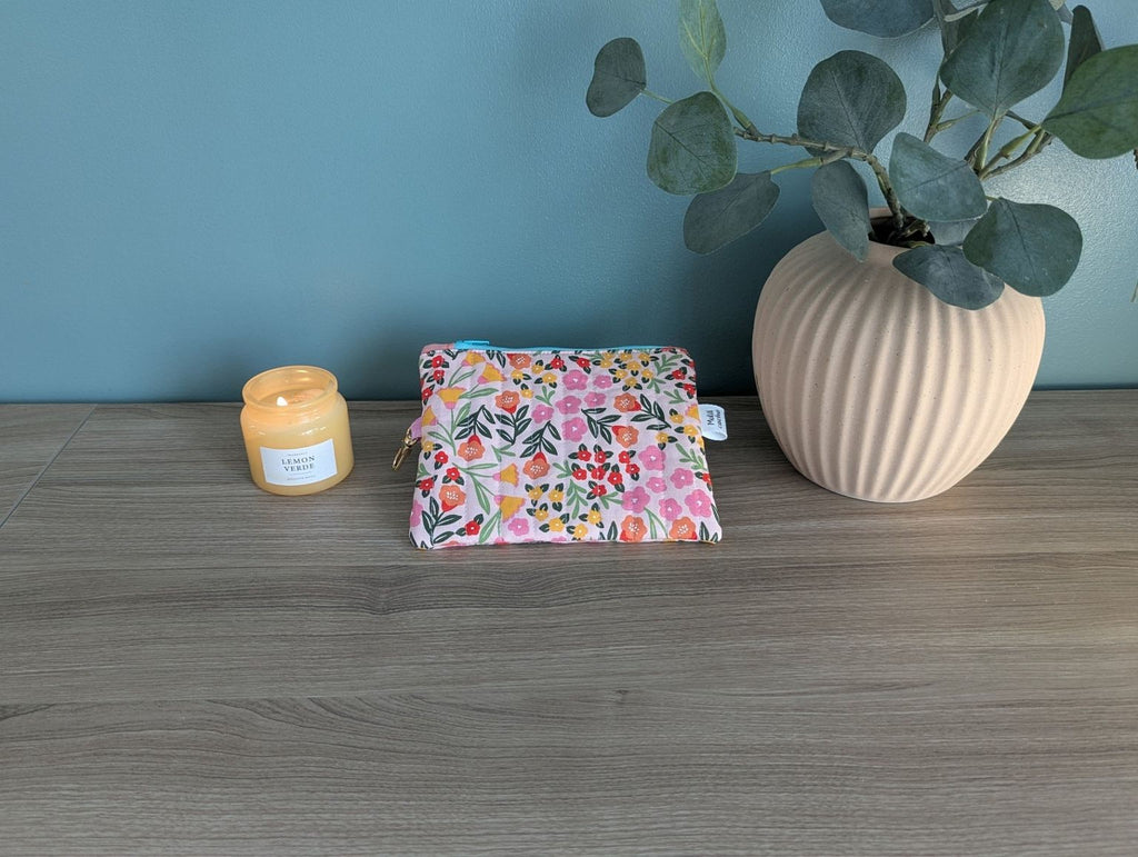 A wooden table with a floral patterned bag, a candle, and a potted plant.