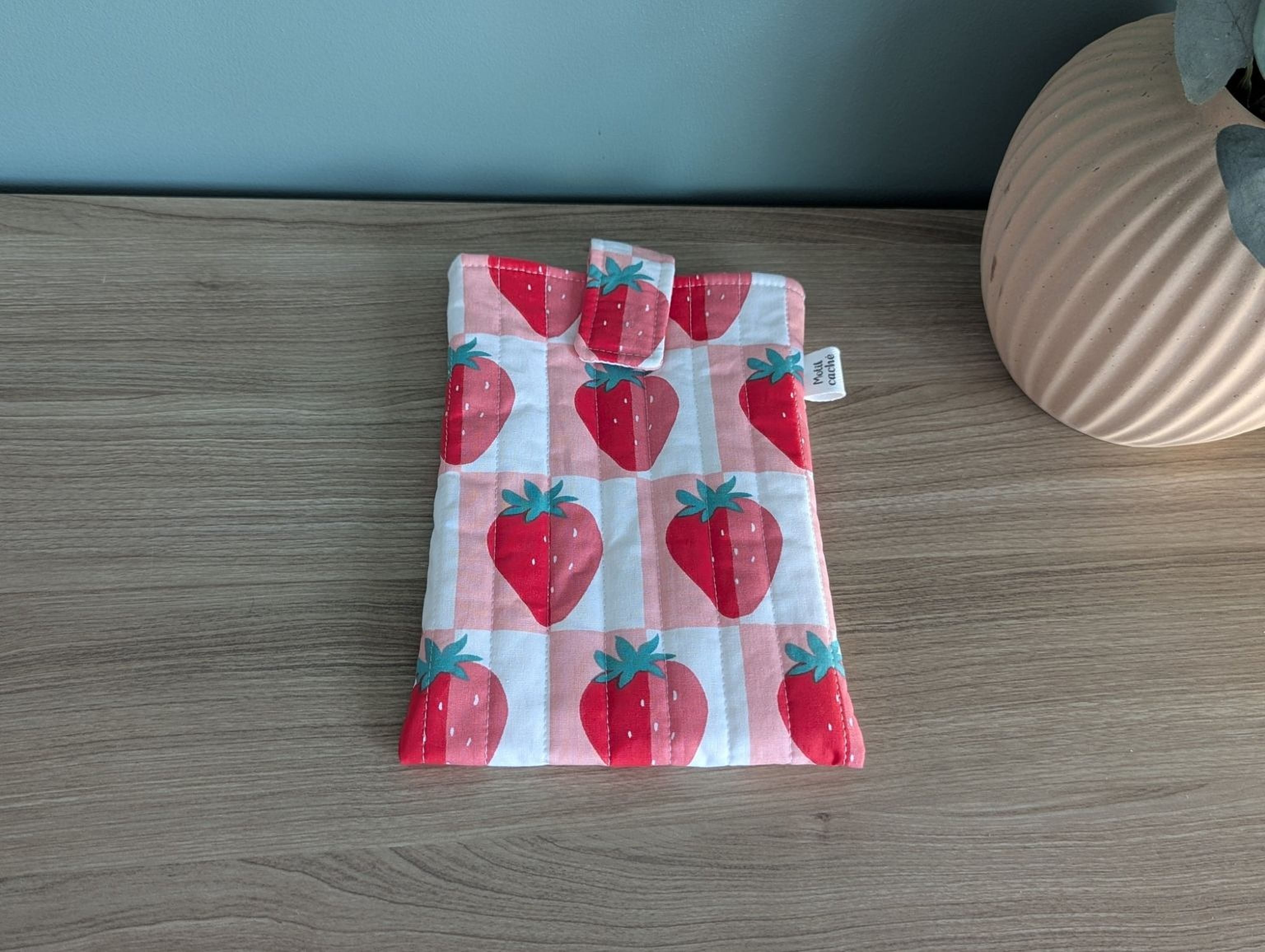 A wooden table with a white and pink quilted bag featuring a repeating pattern of red strawberries.