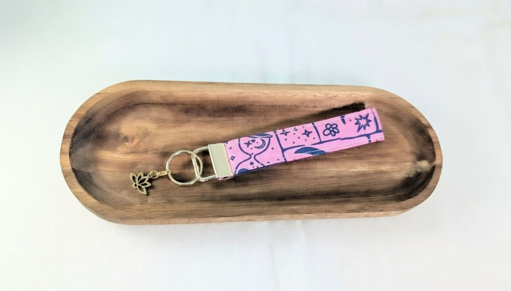 A wooden tray with a pink keychain featuring a floral design and a small charm attached to it.