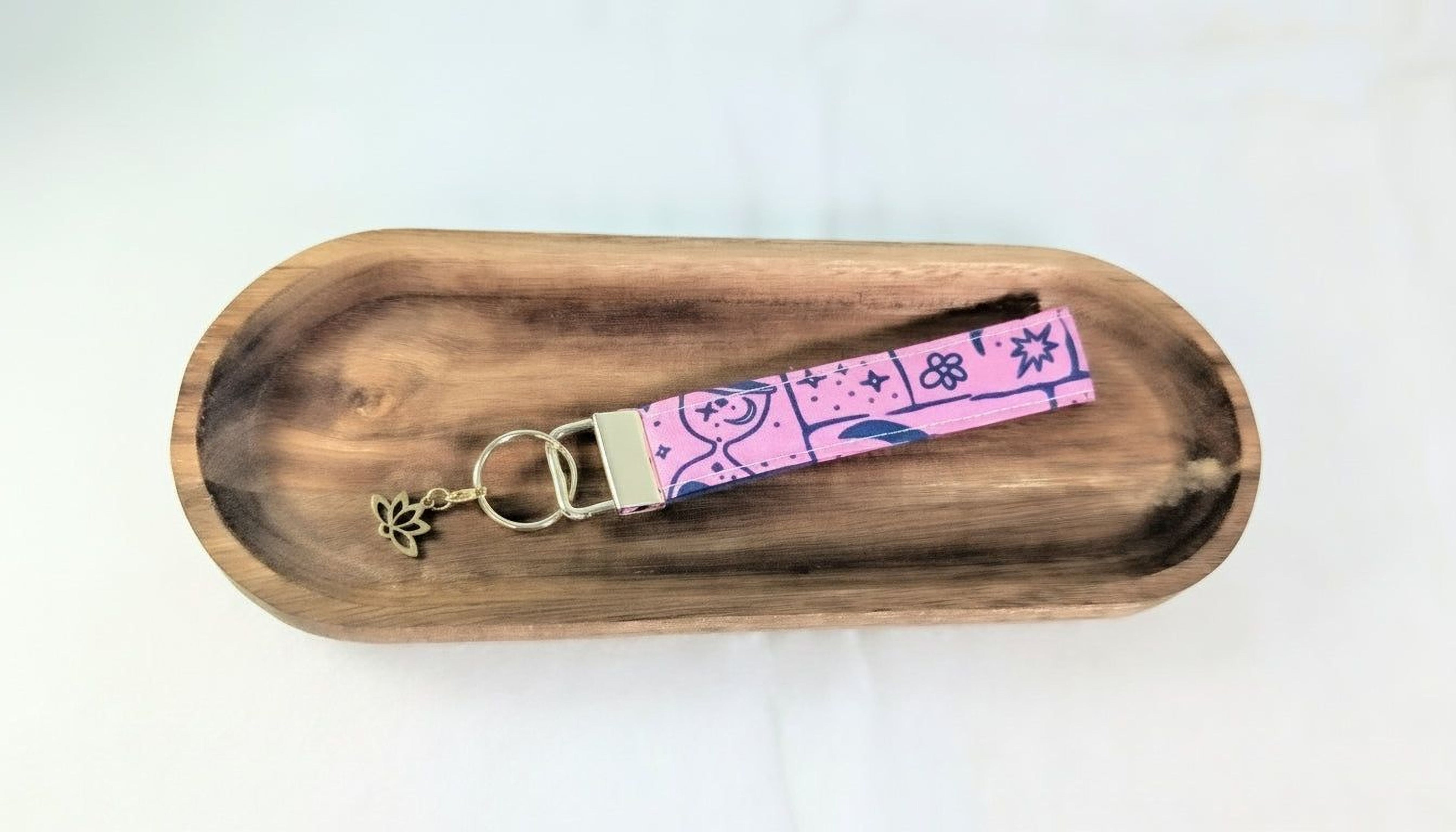 A wooden tray with a pink keychain featuring a floral design and a small charm attached to it.