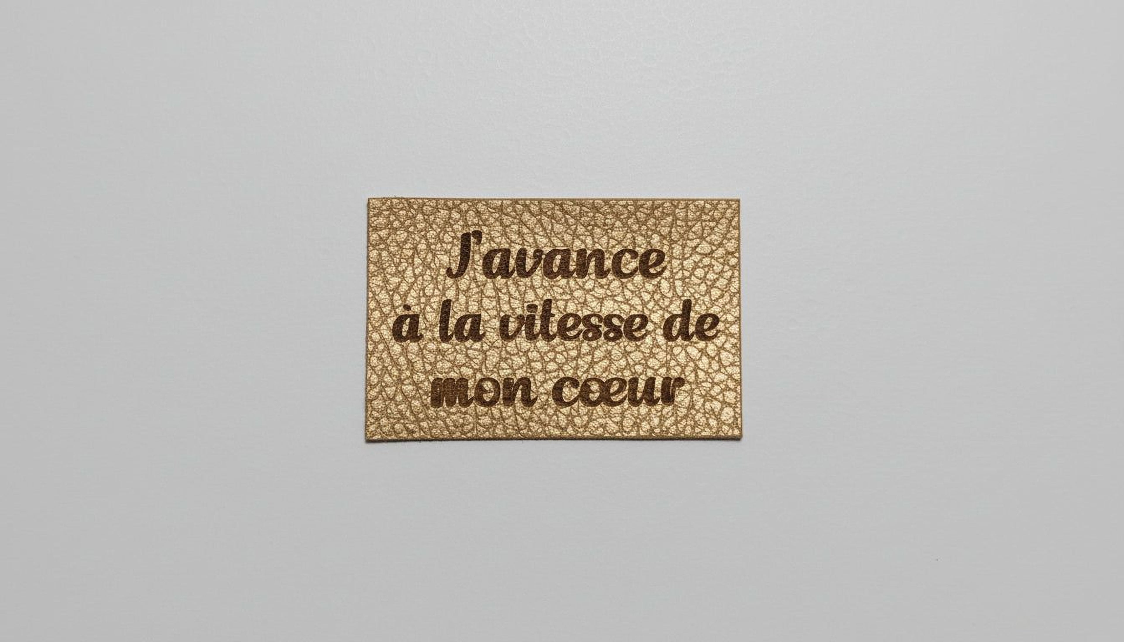 a rectangular, gold-colored label with the text "Savance a la vitesse de mon céeur" printed on it.