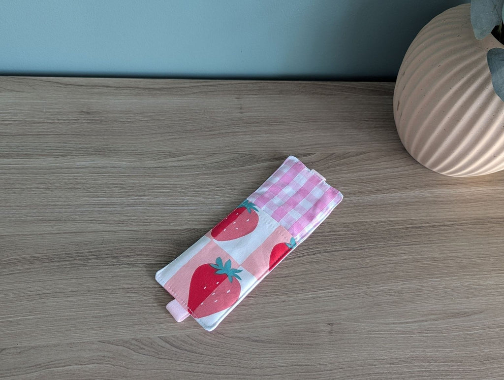A wooden table with a pink and white striped cloth featuring a strawberry pattern, a small vase, and a pink ceramic object.