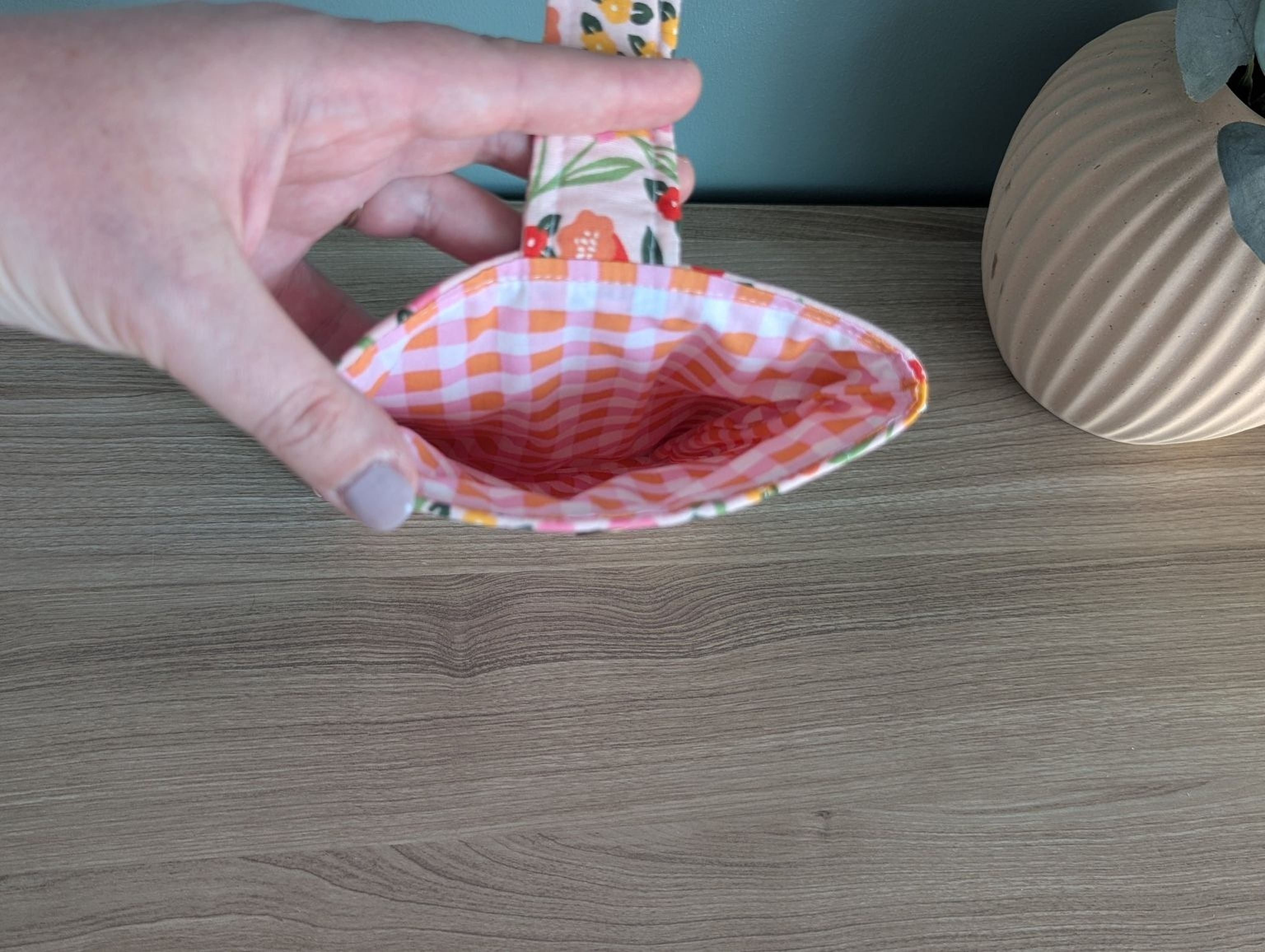 A hand holding a colorful, patterned fabric with a floral design, placed on a wooden surface next to a vase.