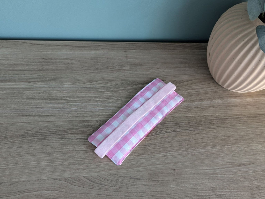 A pink and white checkered cloth is placed on a wooden surface next to a vase.