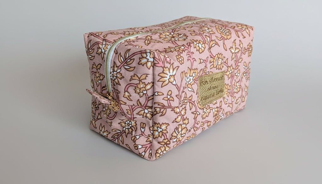 A pink floral-patterned cosmetic bag with a zipper closure and a small gold-colored label on the side.