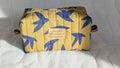 A yellow and blue quilted bag with a bird pattern, featuring a small label with text on it.