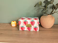 A wooden table with a pink vase, a candle, and a red and white striped bag with a strawberry pattern.
