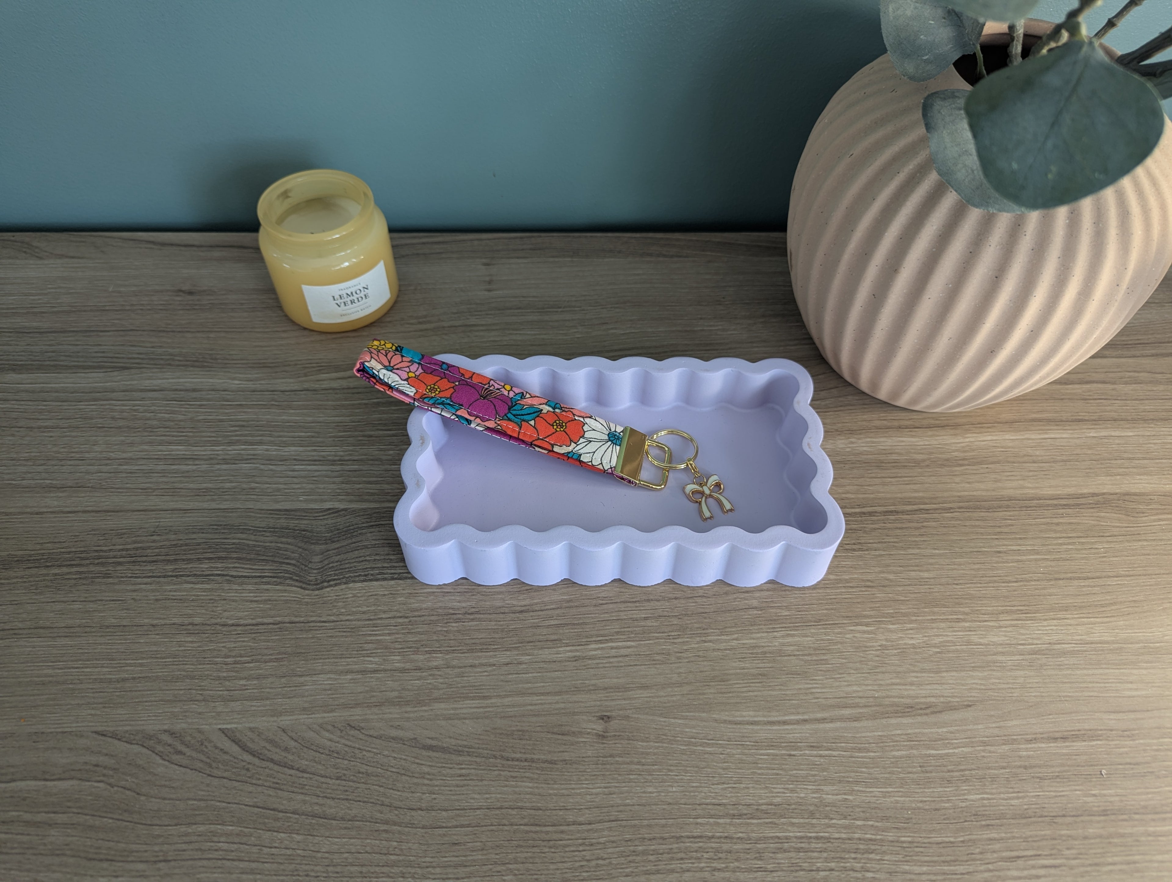 a wooden table with a white tray, a colorful keychain, a small jar, and a vase with a plant.