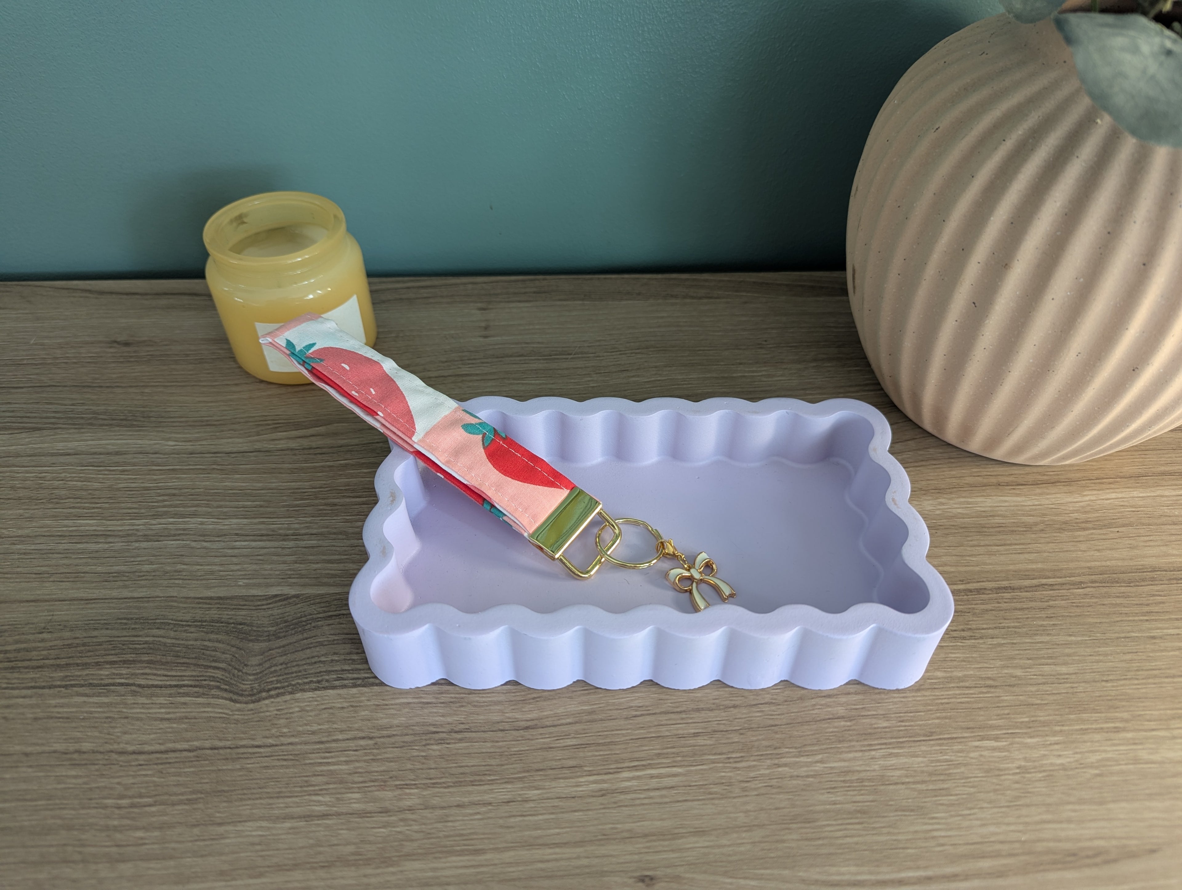 a white, scalloped tray with a keychain attached to it, placed on a wooden surface next to a small vase and a jar.