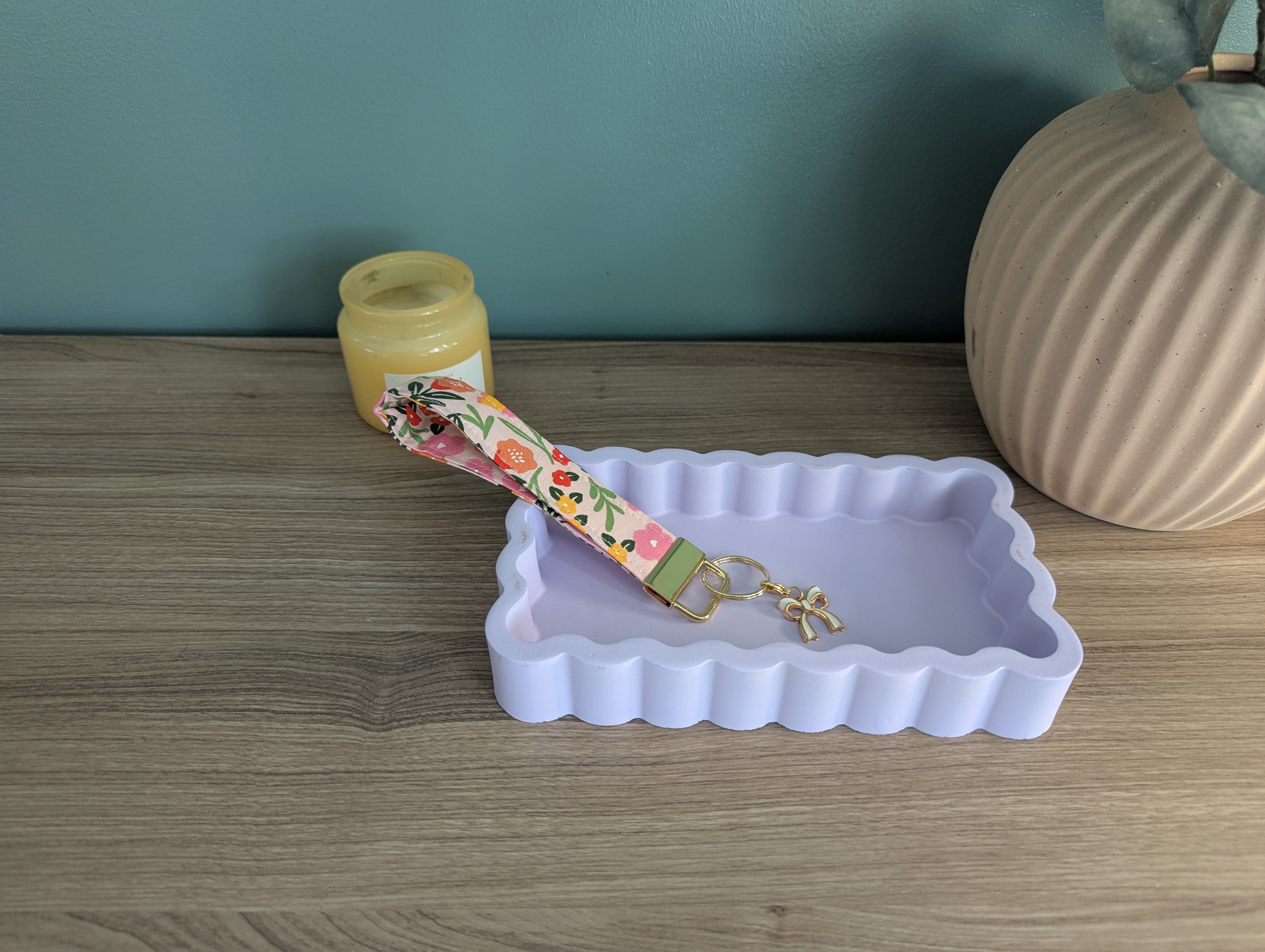 a wooden table with a white rectangular tray, a small yellow jar, and a pink keychain with a floral design.
