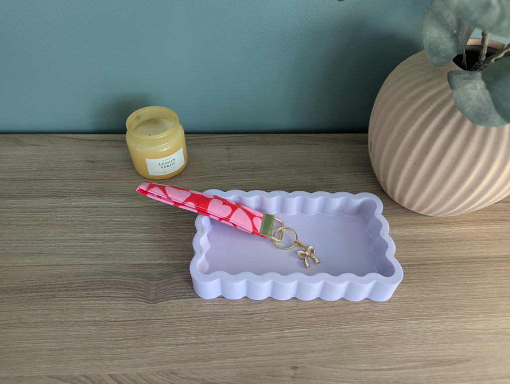 a wooden table with a white rectangular tray, a pink heart-shaped keychain, and a small jar of honey.