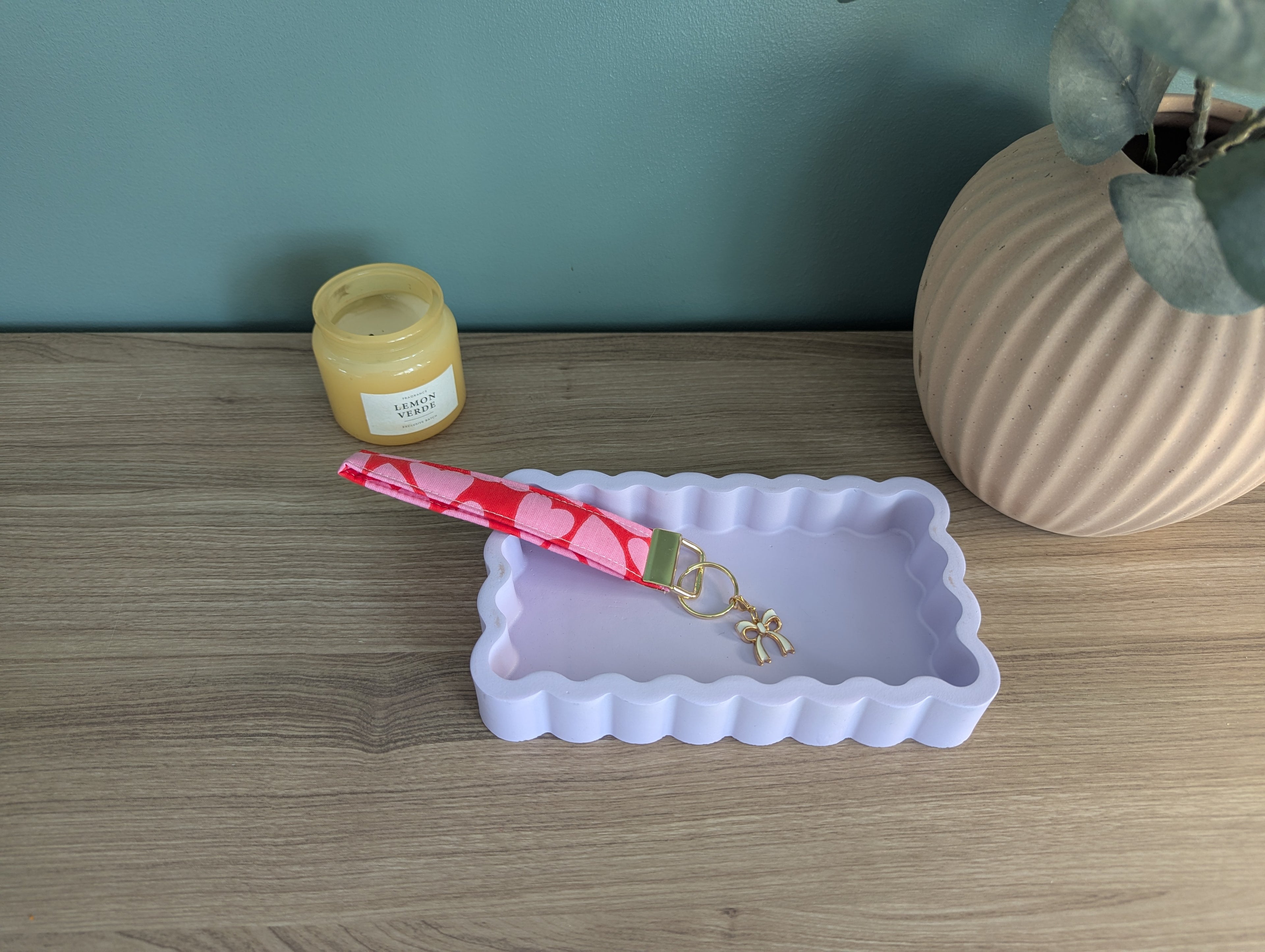 a wooden table with a white rectangular tray, a pink heart-shaped keychain, and a small jar of honey.