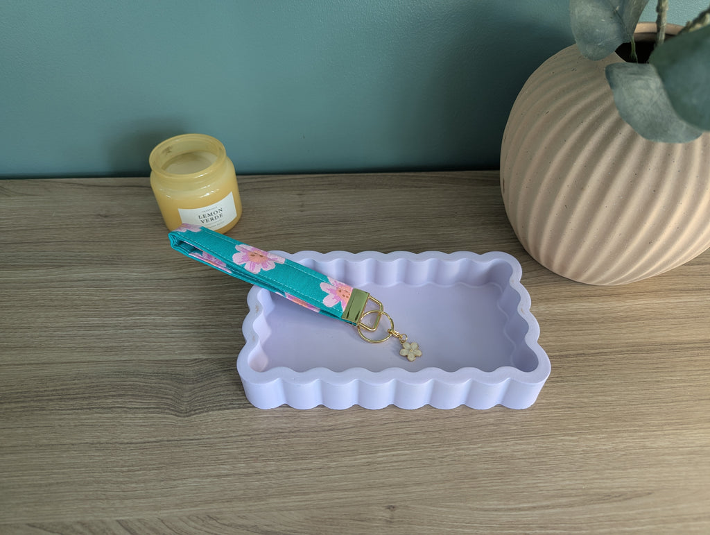a wooden table with a white rectangular tray, a blue and pink floral keychain, a small vase, and a jar of honey.