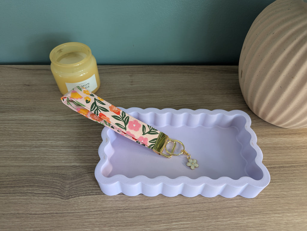 a pink and green floral keychain resting on a white rectangular tray, with a small white flower charm hanging from it.