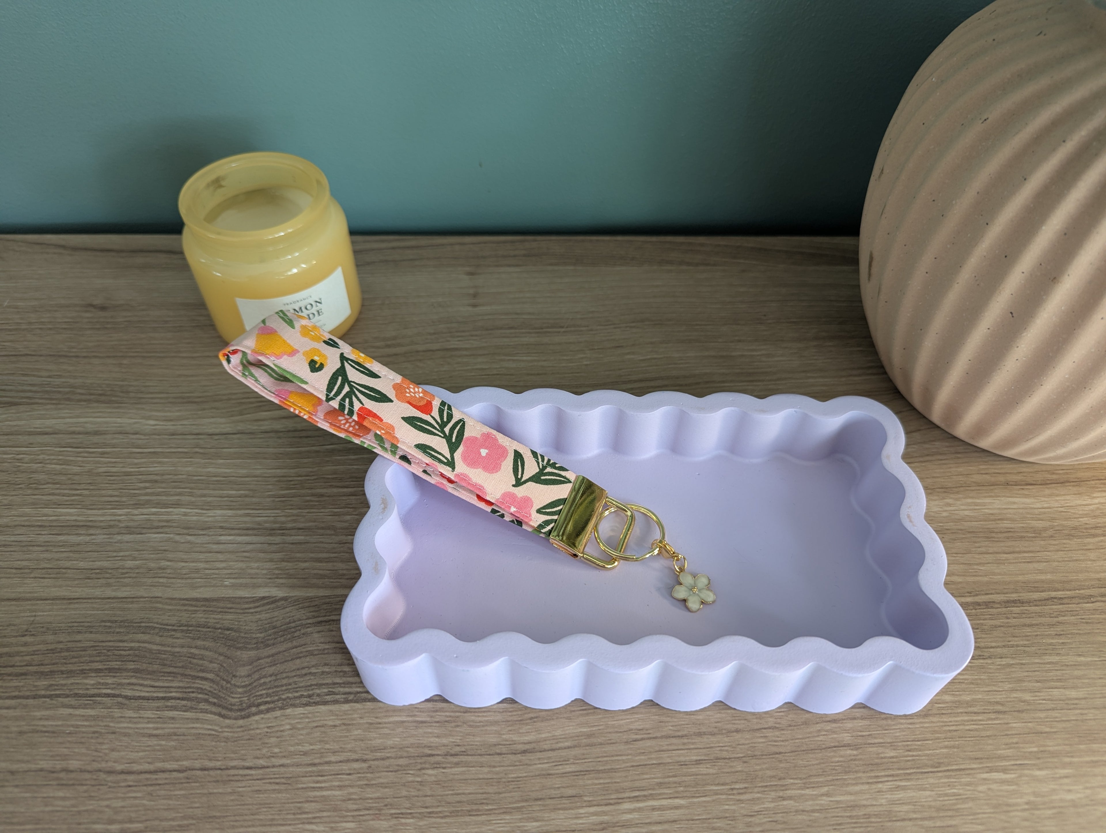 a pink and green floral keychain resting on a white rectangular tray, with a small white flower charm hanging from it.