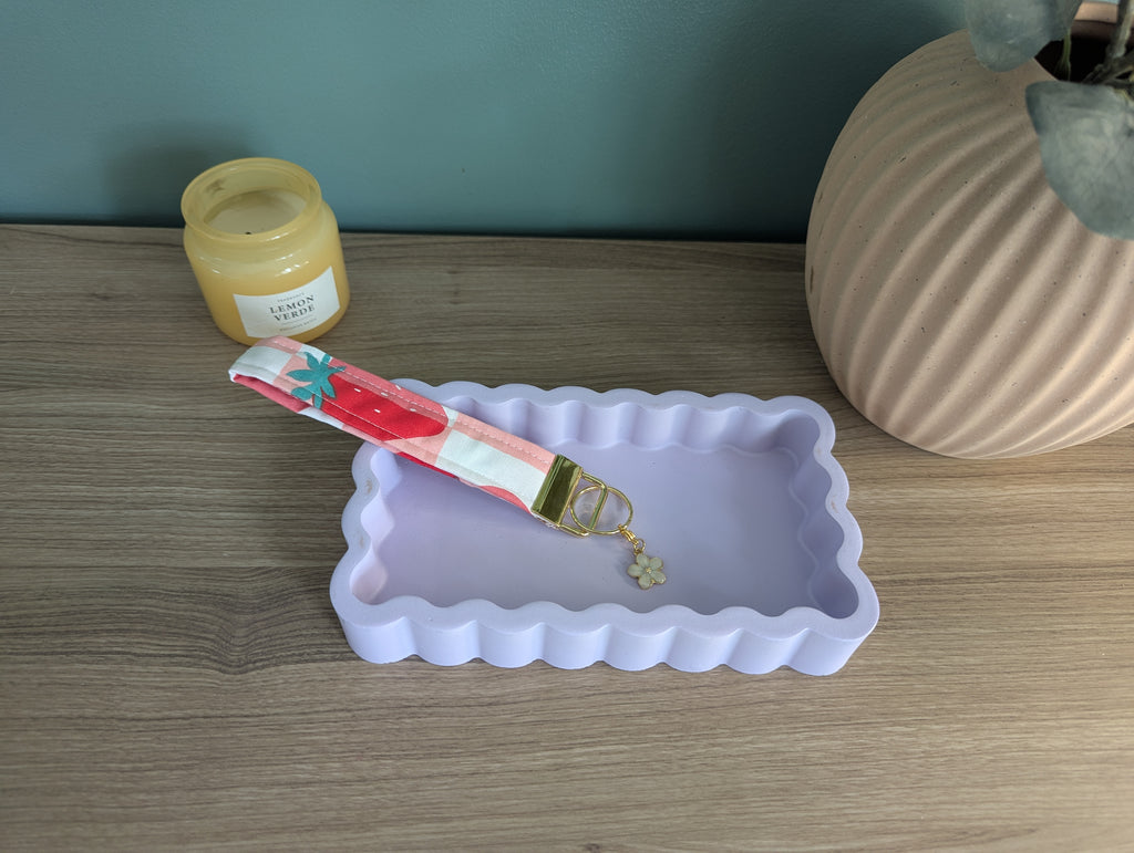 a pink and white scalloped tray, a keychain with a flower charm, and a jar of lemonade on a wooden surface.