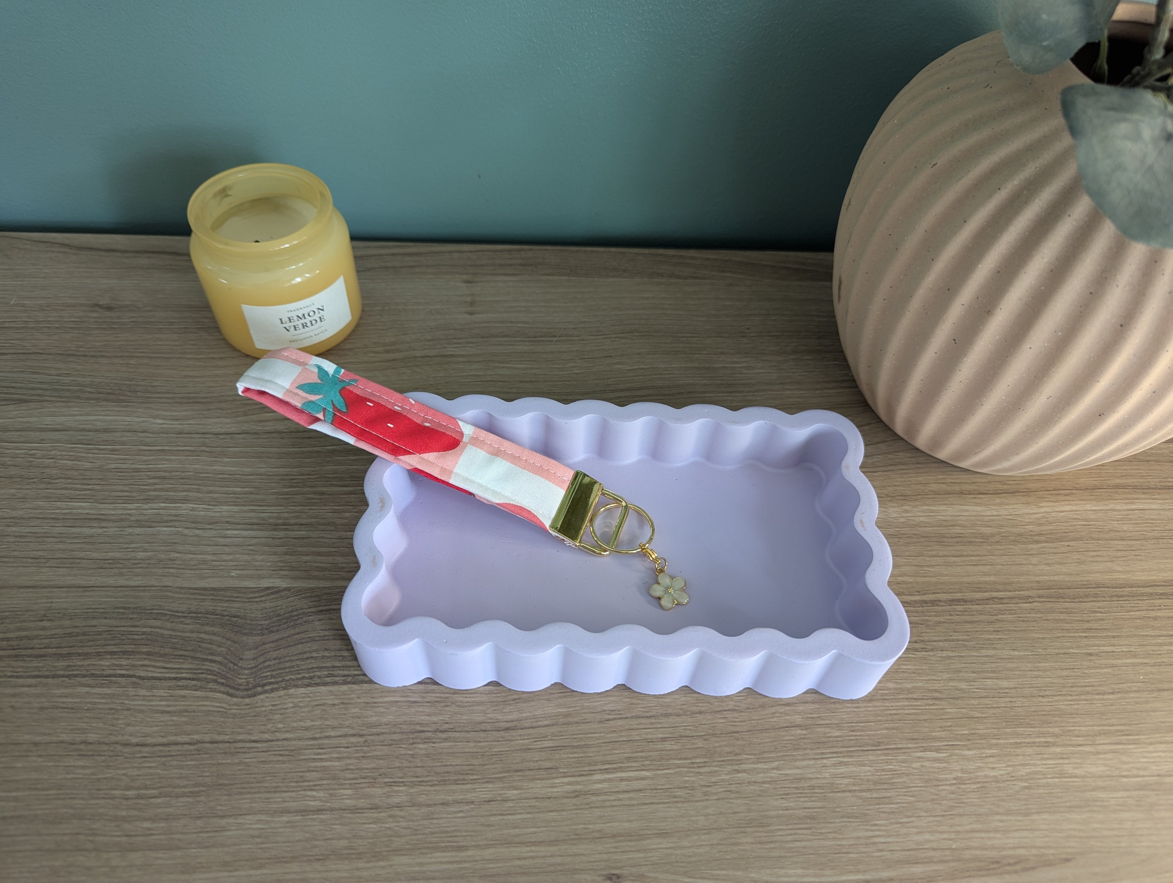 a pink and white scalloped tray, a keychain with a flower charm, and a jar of lemonade on a wooden surface.