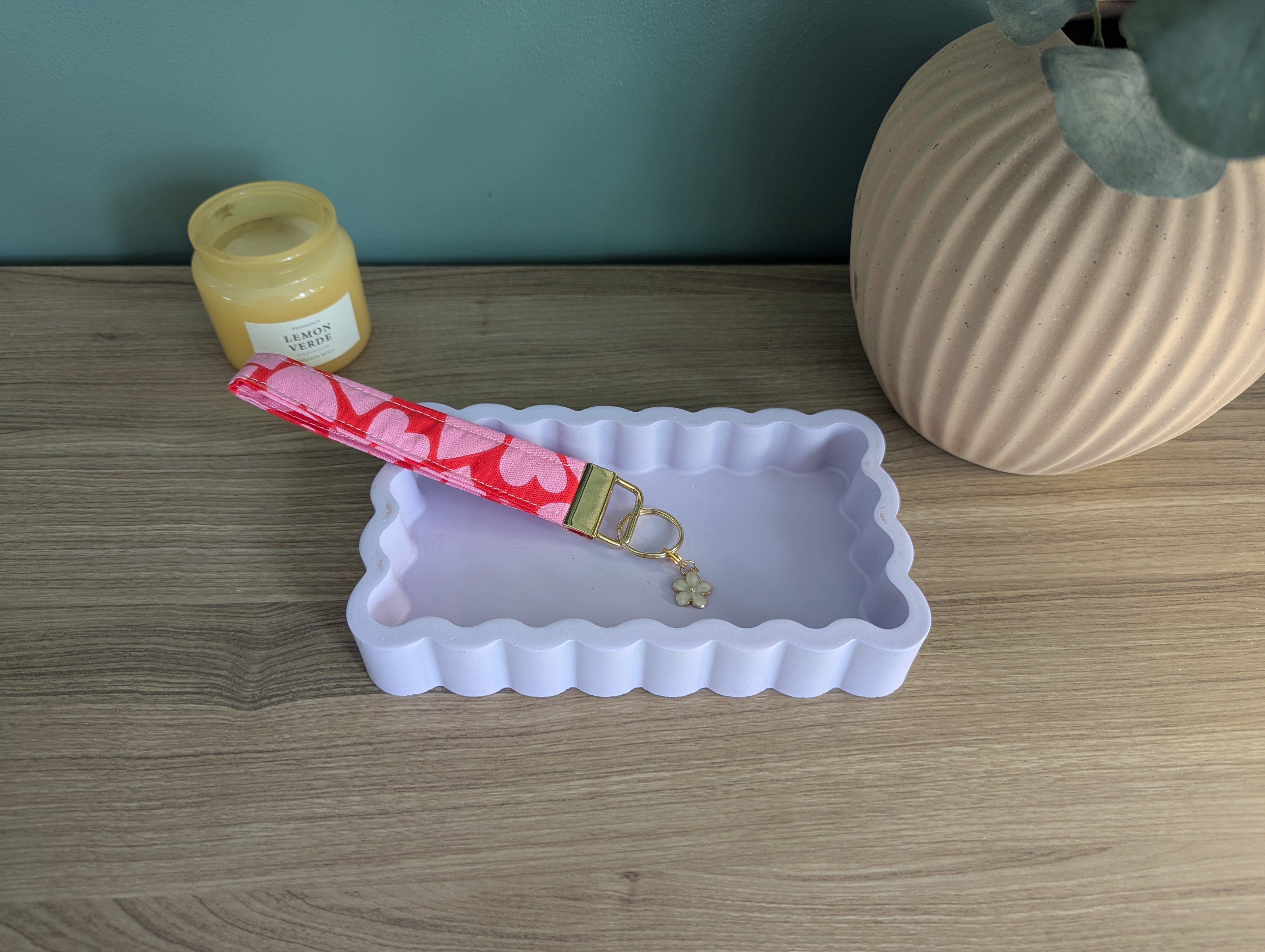 a pink keychain with a heart-shaped charm resting on a white rectangular tray, placed on a wooden surface.
