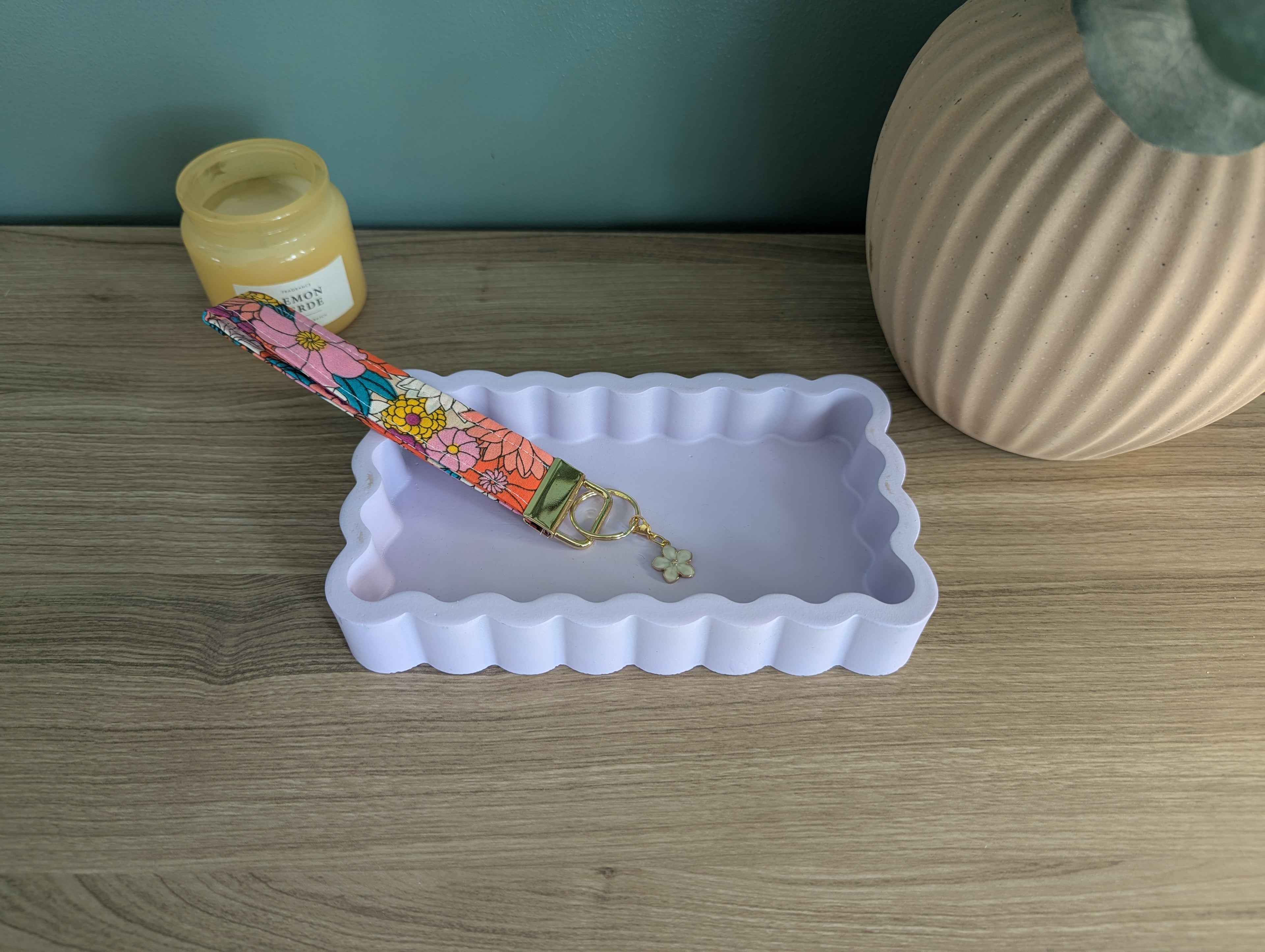 a white rectangular tray with a colorful floral keychain resting on it, placed on a wooden surface.