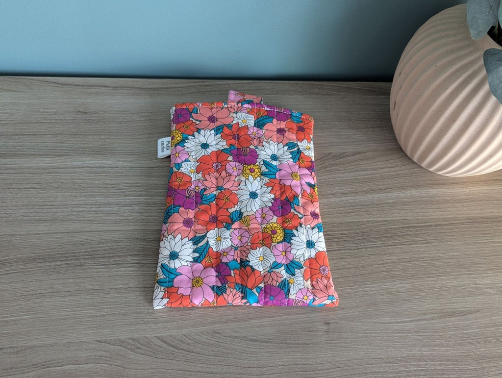 A colorful floral patterned bag or pouch is placed on a wooden surface next to a vase.
