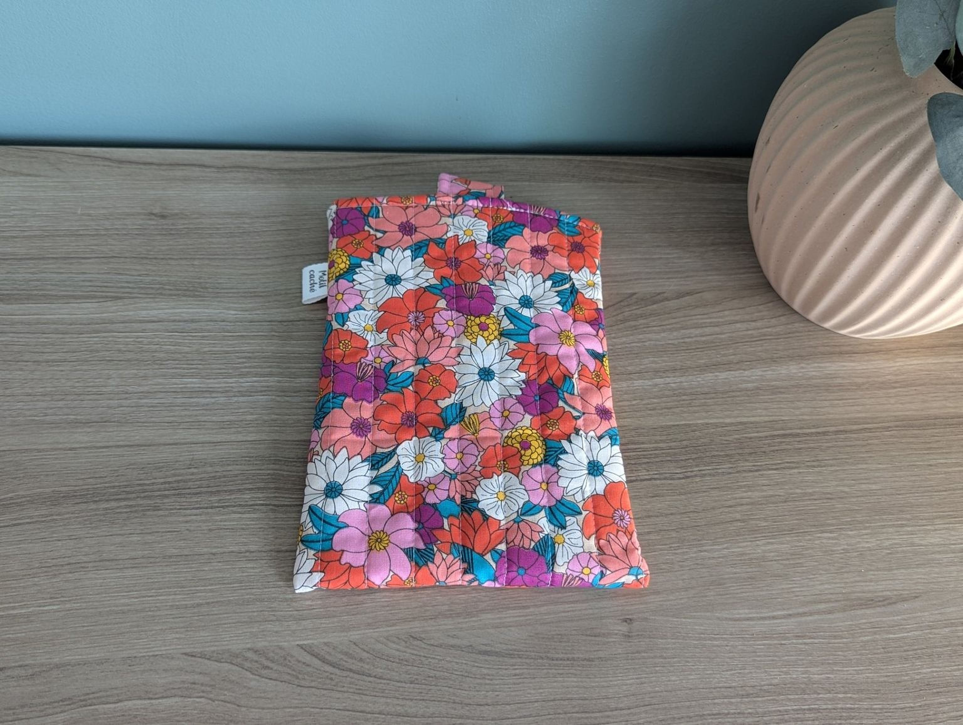 A colorful floral patterned bag or pouch is placed on a wooden surface next to a vase.