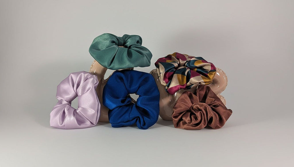 A collection of colorful hair accessories, including scrunchie ties and hair ties in various pastel shades, arranged on a plain background.