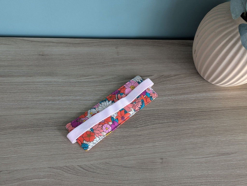 A floral patterned fabric item, possibly a cloth or a decorative piece, is placed on a wooden surface next to a vase.