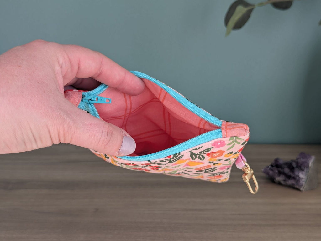 A hand holding a colorful floral-patterned coin purse with a zipper closure.