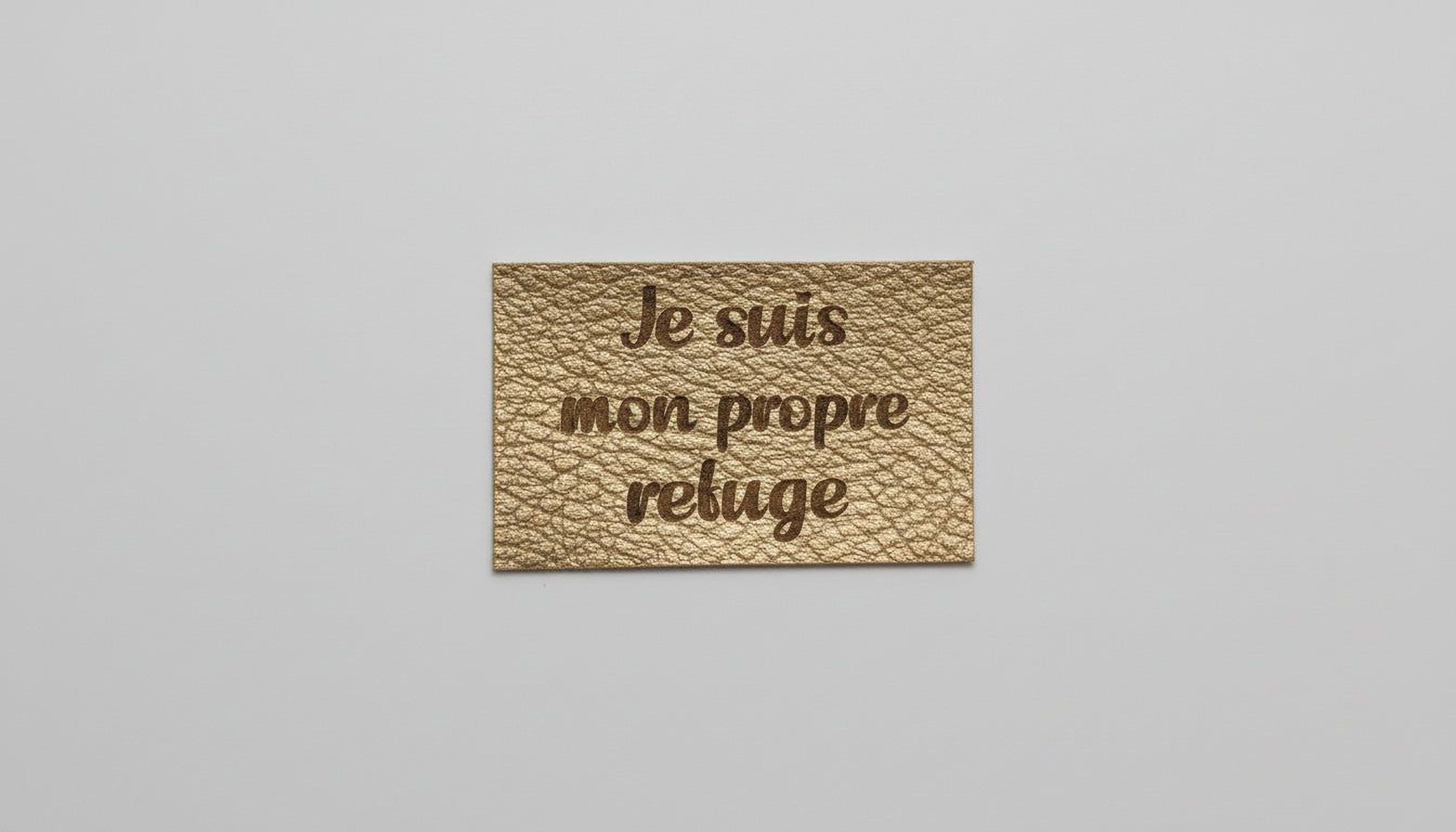A rectangular piece of leather with the text "Je suis mon prope refuge" engraved on it.