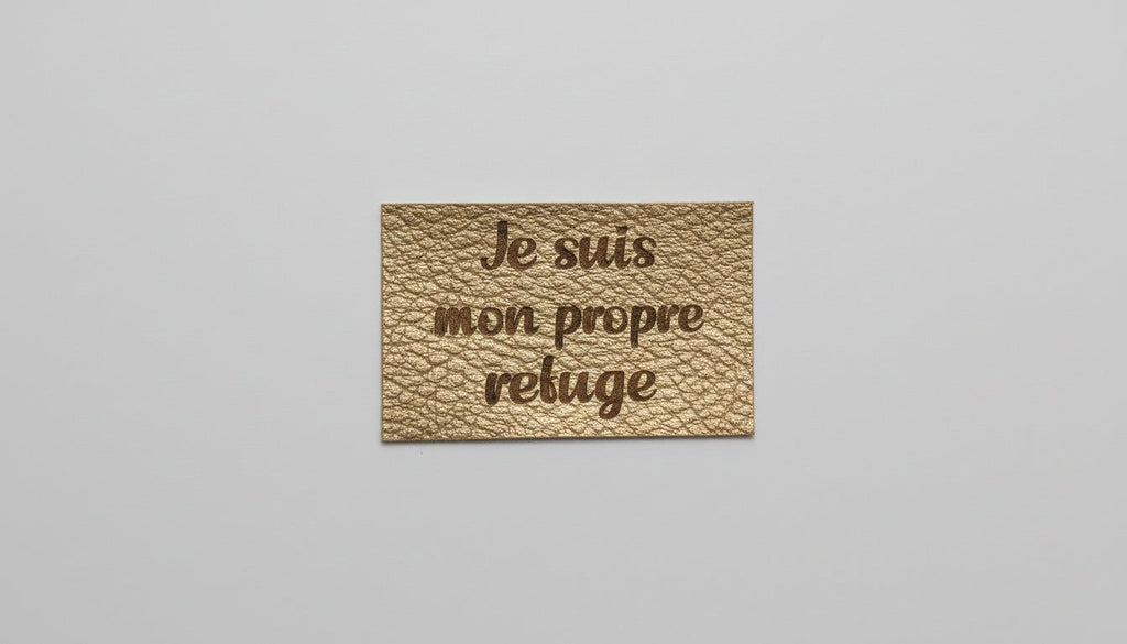 A rectangular piece of leather with the text "Je suis mon prope refuge" engraved on it.